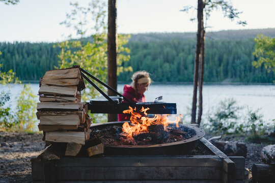 Food being prepared on fire pit while woman sitting in background at forest