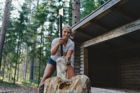 Low angle view of woman chopping wood next to her cabin in forest