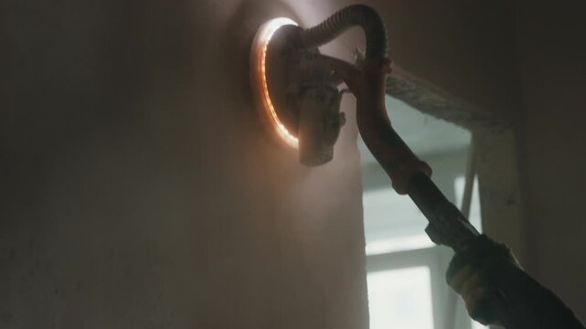 Worker sanding interior wall with electric drywall sander close up