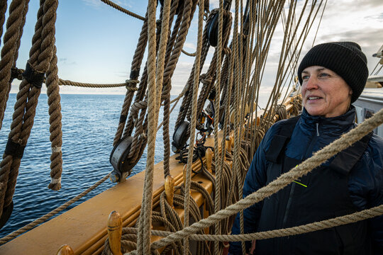 Female sailor looking away while standing on deck of tall ship amidst hemp rope rigging