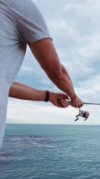 Vertical video. Rear View of Young Woman Fishing With Spinning Rod Above Tropical Ocean Near Rocky Coastline Under Cloudy Sky, Slow Motion Outdoor Recreation