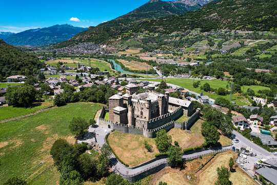 Aerial view of the medieval Fenis Castle with its stone towers and crenellated walls surrounded by green fields and alpine mountains in Fenis, Aosta Valley, Italy.