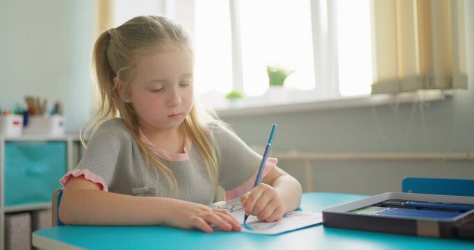 Young schoolgirl concentrating on drawing with a pencil at a classroom desk, surrounded by soft window light and learning materials
