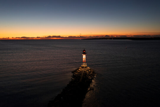 Drone shot of illuminated lighthouse amidst sea against scenic sky at dusk