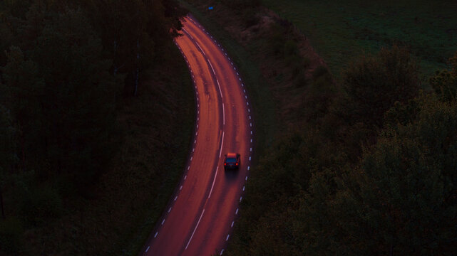 Drone shot of car moving on road surrounded by greenery at night
