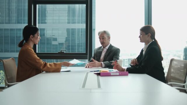 White senior male CEO boss interviews Asian female worker for company employment collaboration and job opportunity with career resume document in office meeting with human resources secretary woman.