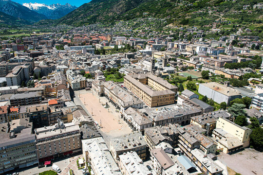 Aerial view of Piazza Chanoux and the historic center surrounded by traditional rooftops and the majestic snow-capped Alps under a clear blue sky Aosta, Aosta Valley, Italy.