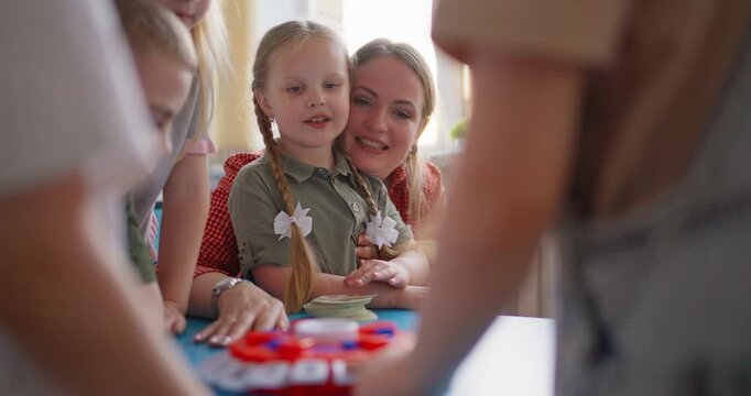 Smiling teacher and young children gathered around a table playing a colorful educational game in a bright daycare classroom