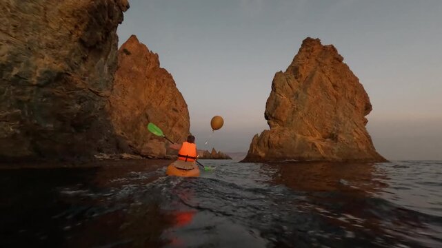 Kayaking ocean adventure, man paddles between dramatic sea rocks at sunset, exploring rugged coastline