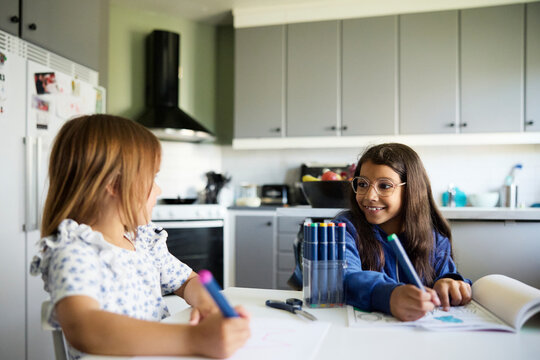 Smiling girl coloring in book with sister while sitting at table in home