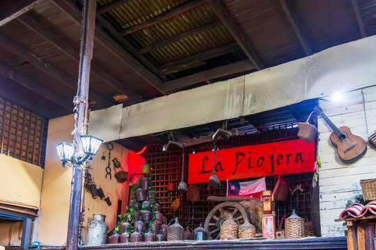 Vintage decor fills a corner of La Piojera in Santiago, where woven bottles, rustic tools, and a Chilean flag sit beneath the tavern&rsquo;s iconic sign, capturing the bar&rsquo;s historic character