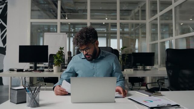 Irritated stressed Arabian business man working with papers throwing documents away holding head laptop work problem failure ethnic businessman male throw reports crisis guy feeling headache in office