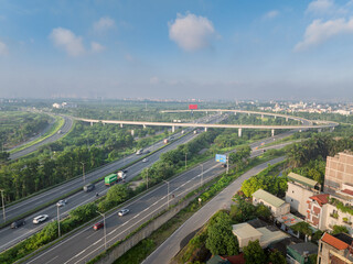 Obraz premium Morning aerial view of Co Linh interchange on Hanoi Ring Road 3 with elevated ramps, light traffic, urban outskirts, and clear blue sky.