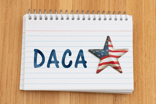 DACA text on a spiral notebook of index cards with USA flag star on wood desk