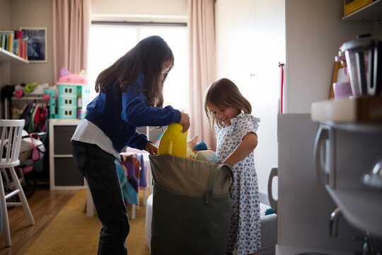 Sisters filling bag with toys in bedroom at home