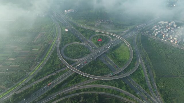 High altitude drone footage of Co Linh interchange surrounded by drifting clouds, green landscape, and complex elevated highway infrastructure in Hanoi.