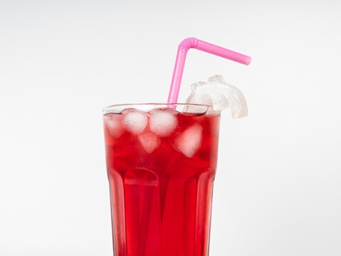 Refreshing ice cold red cocktail drink in a tall glass with ice cubes and a pink plastic straw. Minimalist product shot isolated on a clean white background. Concept of summer fruit juice, beverage