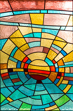 Beautiful stained glass window texture with a circular geometric pattern. Colorful glass mosaic panel backlit by warm sunlight, featuring vibrant blue, red, gold, and orange segments. Abstract art
