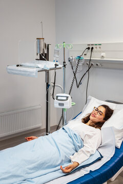 Smiling woman lying on bed next to equipment in hospital ward room