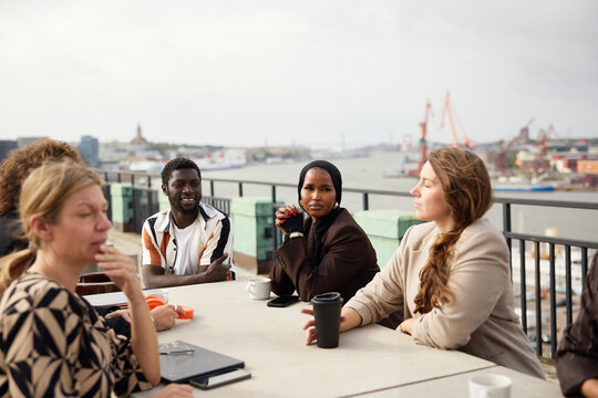 Female entrepreneur in hijab sitting with team mates around table on office terrace