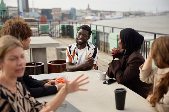 Smiling male entrepreneur interacting with coworkers sitting around table on office terrace
