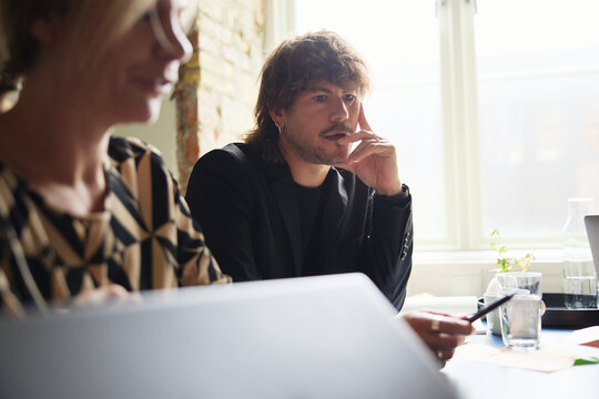 Thoughtful male entrepreneur with hand on chin attending team meeting at office