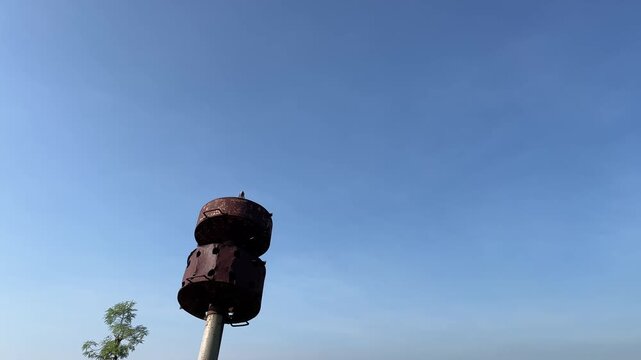Close-up of ancient rusty warning siren against blue sky in rural Asia, highlighting historical relic with dramatic nostalgic atmosphere during dry season.