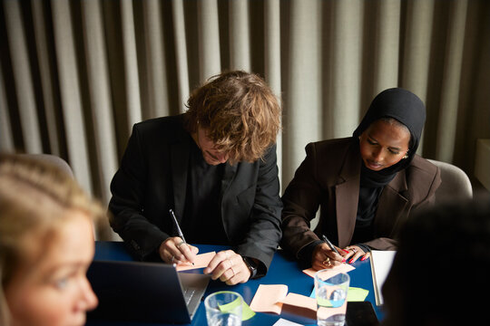High angle view of male and female coworkers writing ideas on adhesive notes while attending office meeting