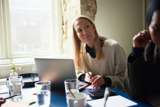 Businesswoman with blond hair peeking at colleague while attending meeting at office