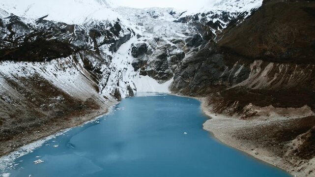 An aerial view of a turquoise glacial lake at the foot of an icefall surrounded by snowy moraine slopes in the Manaslu region of Nepal.