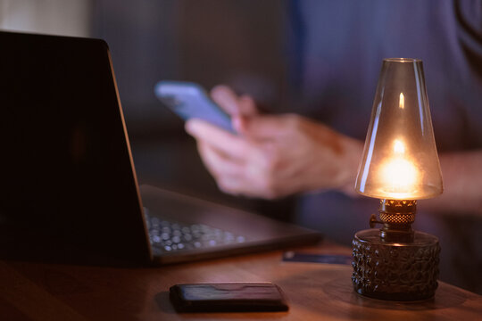 Illuminated lantern on table with man using smart phone in background