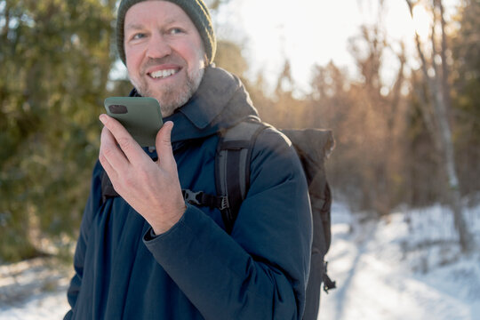 Smiling man talking through speaker phone while traveling in winter