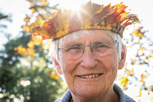 Close-up shot of smiling senior woman wearing crown made of autumn leaves