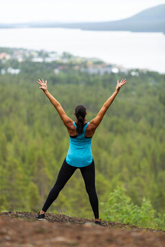 Rear view of woman standing with arms raised on cliff