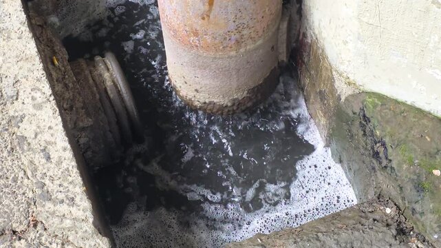 Contaminated water overflowing from a concrete pipe in an urban drainage system, creating foam and pollutants, illustrating environmental damage and industrial waste discharge issues