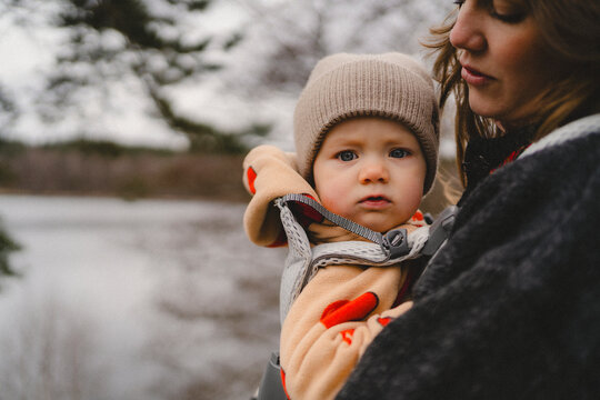 Portrait of cute male toddler wearing knit hat inside carrier carried by mother
