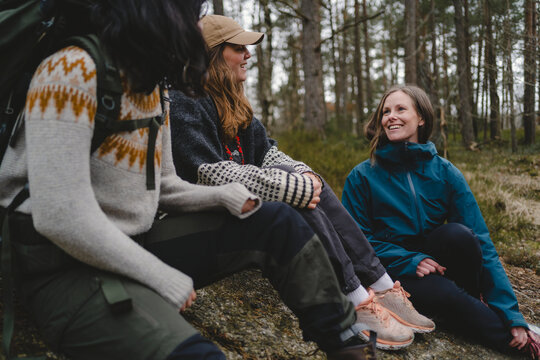 Smiling woman spending leisure time with female friends while sitting on ground in forest