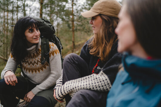Smiling female backpacker talking with friends while sitting in forest during hiking travel