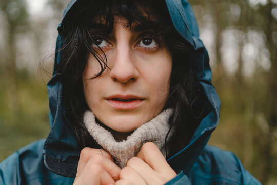 Woman wearing hooded raincoat shivering in rain
