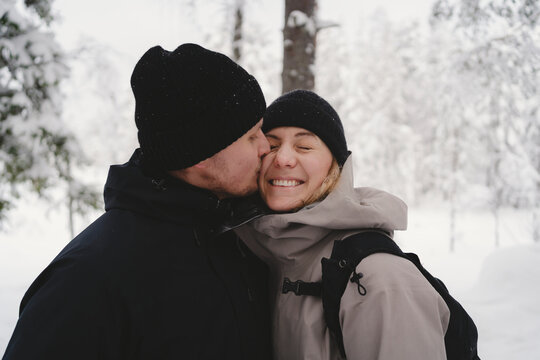 Romantic man kissing woman wearing winter jacket in forest
