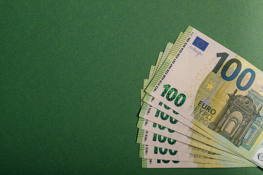 Fan of one hundred euro banknotes arranged on a dark green surface.