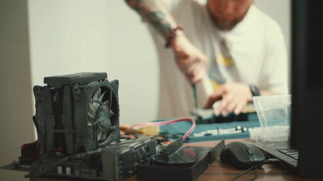 Tech enthusiast repairs computer parts with tools on a wooden table in a well-lit room during daytime