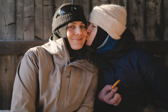 Girl kissing her mother sitting in log cabin during winter season