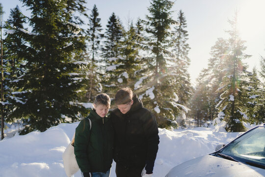 Man and woman dressed in warm clothes standing by car in winter forest