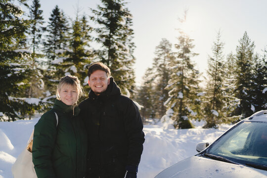 Portrait of smiling couple standing next to car in winter forest