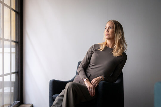 Contemplative female business entrepreneur looking away while leaning on armchair against wall in office
