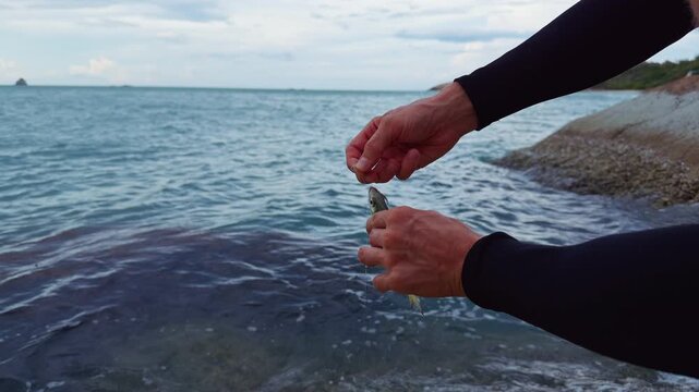 Close View of Hands Removing Freshly Caught Sea Fish From Fishing Hook Near Rocky Tropical Shoreline and Ocean Water, Catch and Release Recreational Fishing