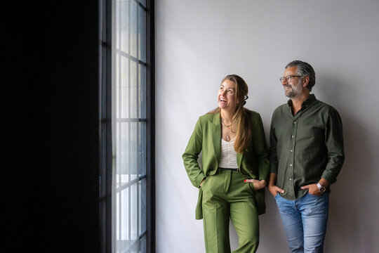 Full length of happy male and female business coworkers looking away while standing with hands in pockets at new office