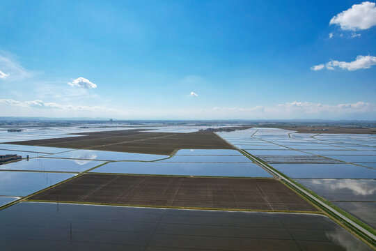 Aerial view of the flooded rice fields at Azienda Agricola Veneria with geometric patterns and blue sky reflections in Veneria, Piemonte, Italy.