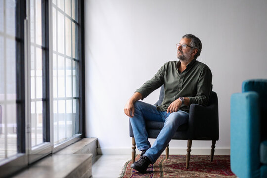Thoughtful mature male business entrepreneur sitting on armchair near window in startup office